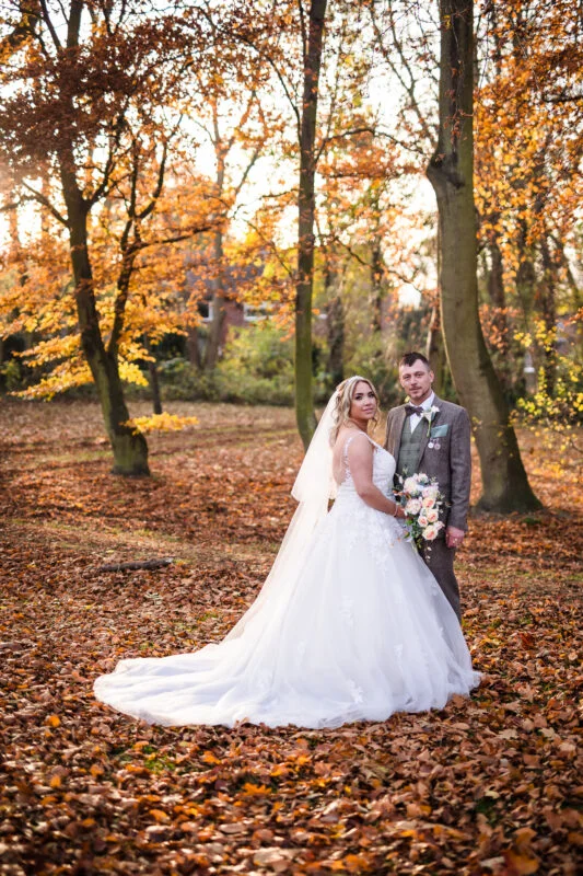 A bride and groom posing in the autumn leaves.