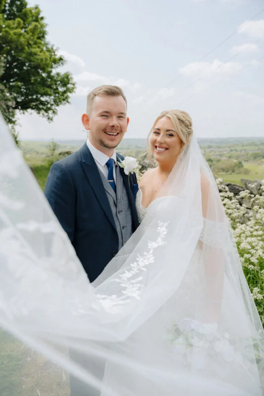 A bride and groom standing under a veil in a field.
