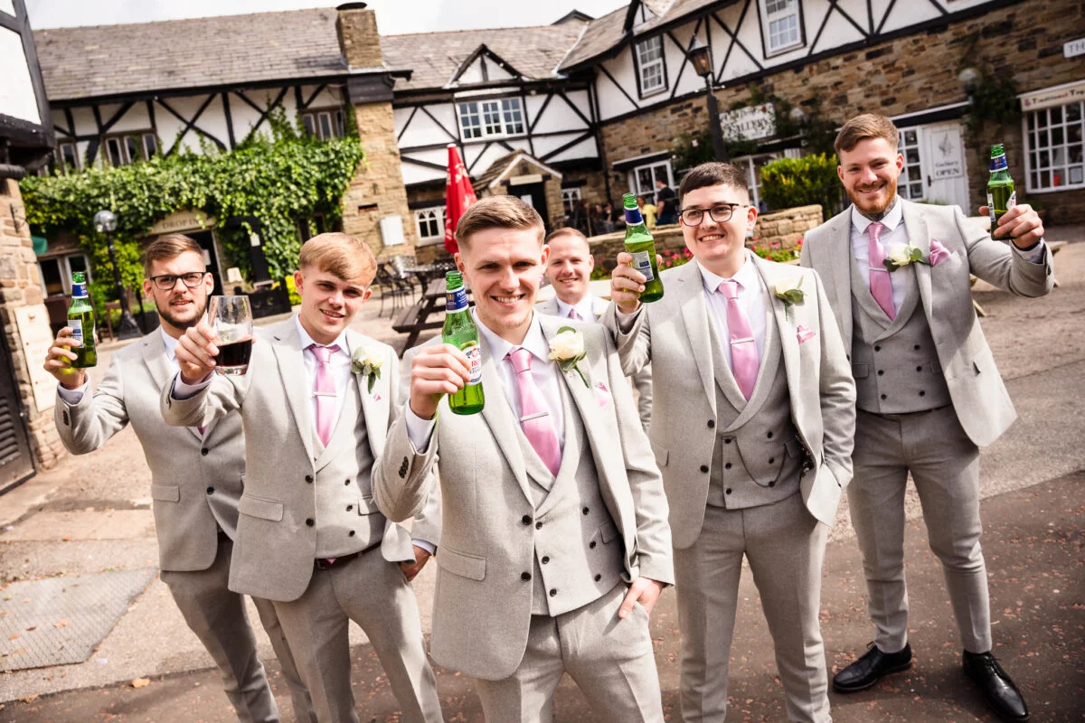 A group of groomsmen holding a beer in front of a building.
