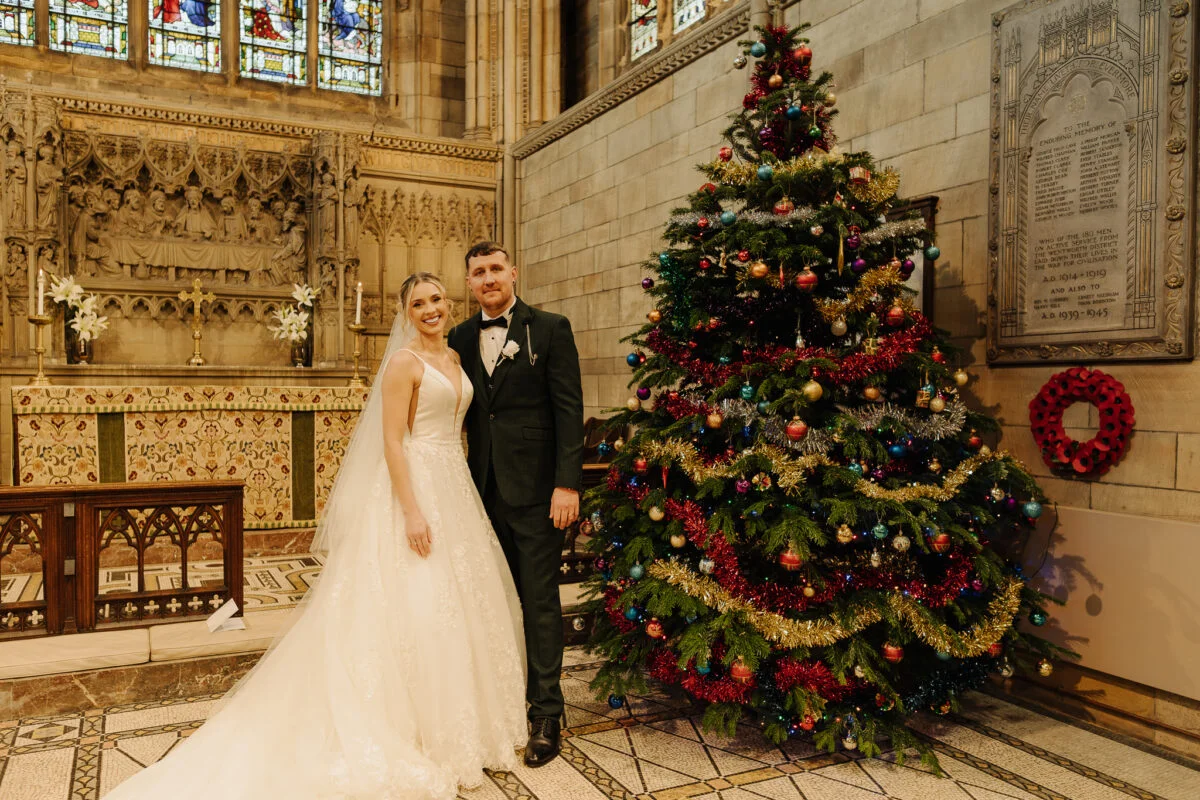 A bride and groom posing in front of a christmas tree.