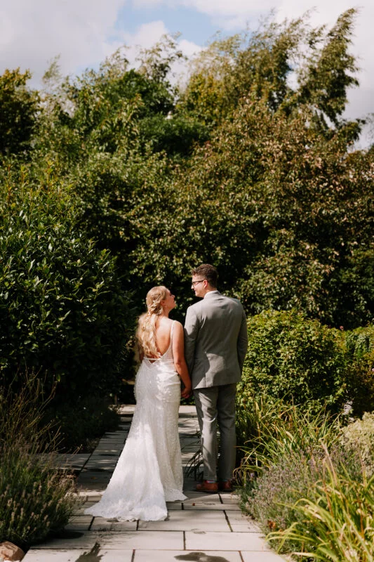 A bride and groom standing on a path in a garden.