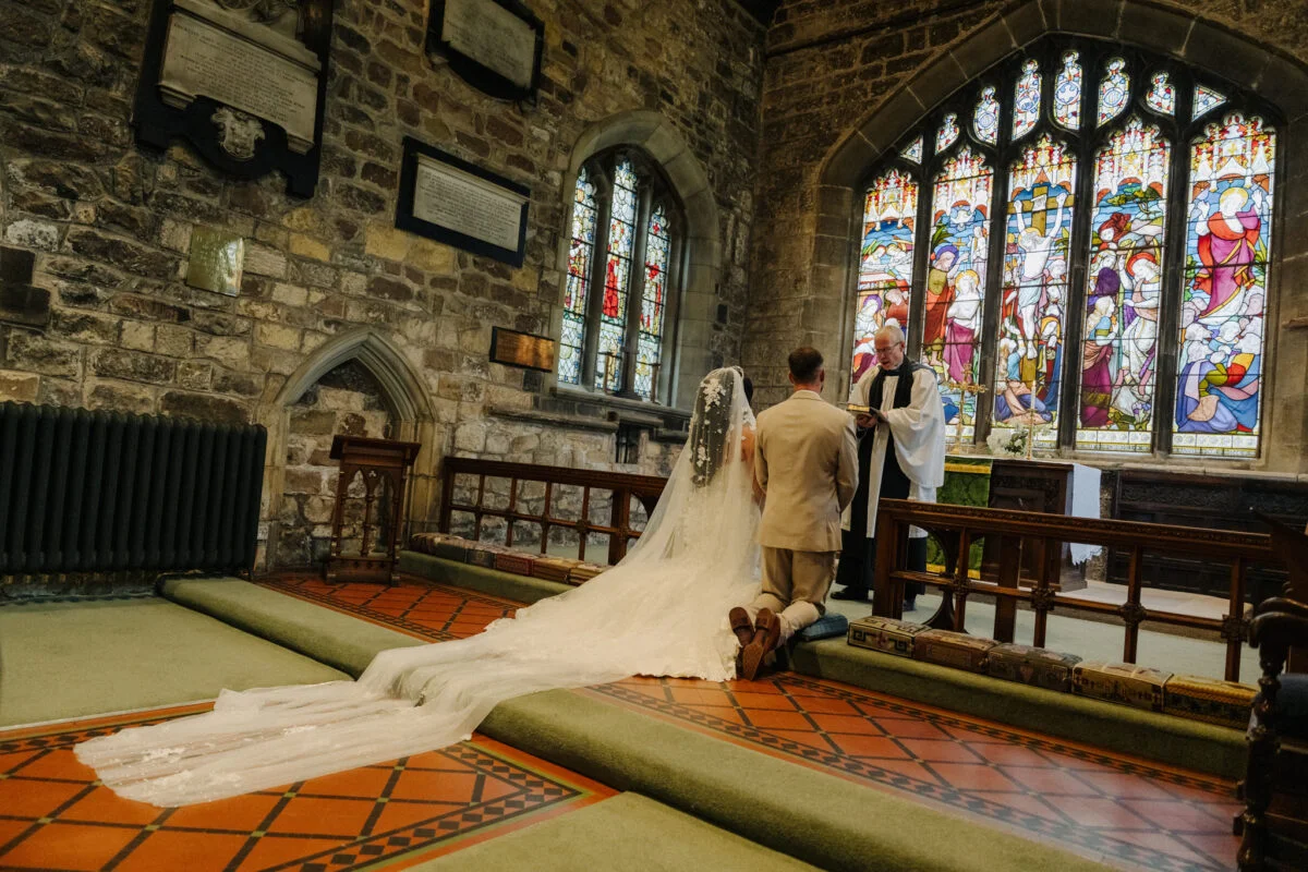 A bride and groom standing in front of a stained glass window.