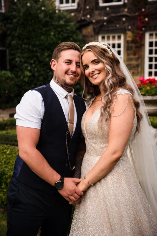 A bride and groom posing for a photo in front of a mansion.