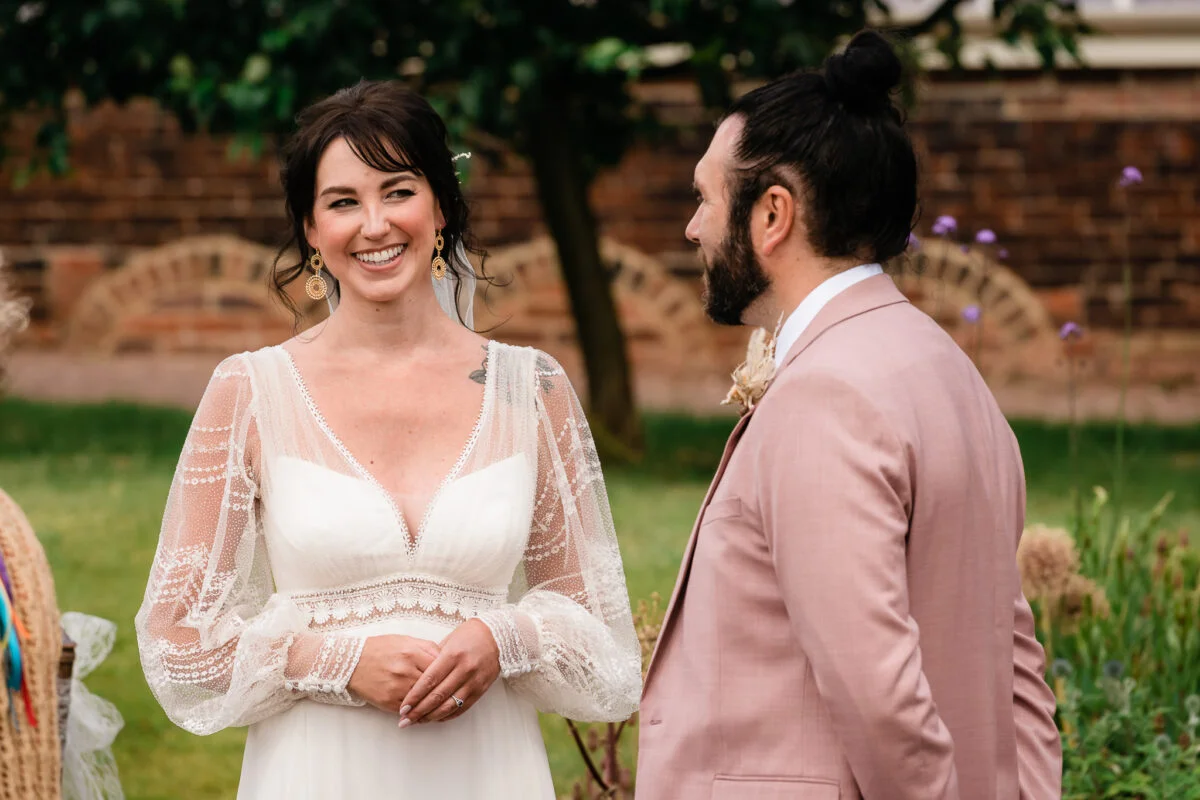A bride and groom smiling at each other in a garden.