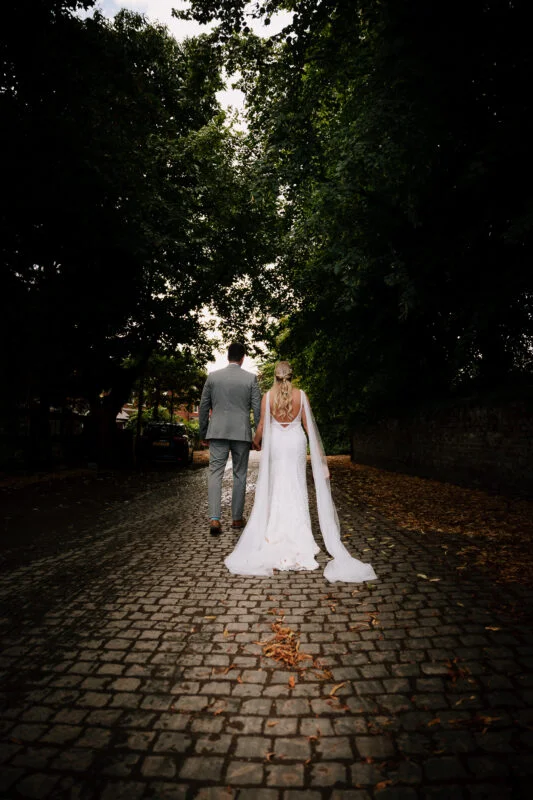 A bride and groom walking down a cobbled path.