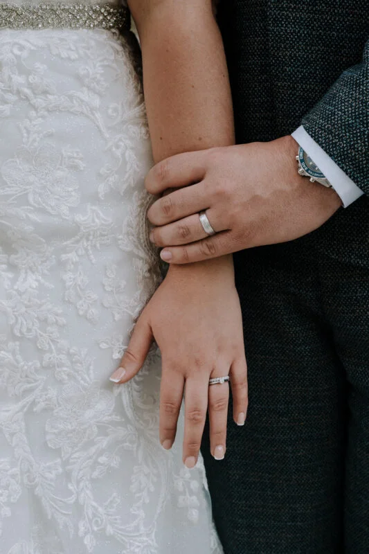 A bride and groom's hands holding each other's wedding rings.