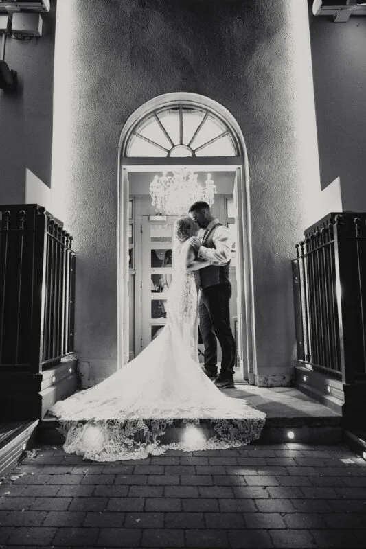 A bride and groom kissing in front of a building at night.
