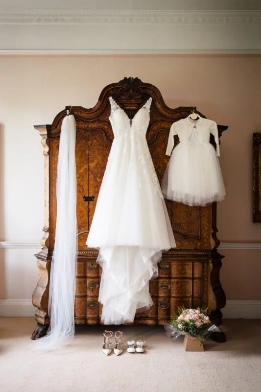 A wedding dress hangs on a dresser in a room.