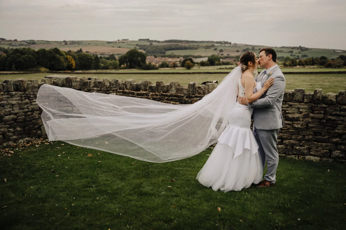 A bride and groom embracing in front of a stone wall.