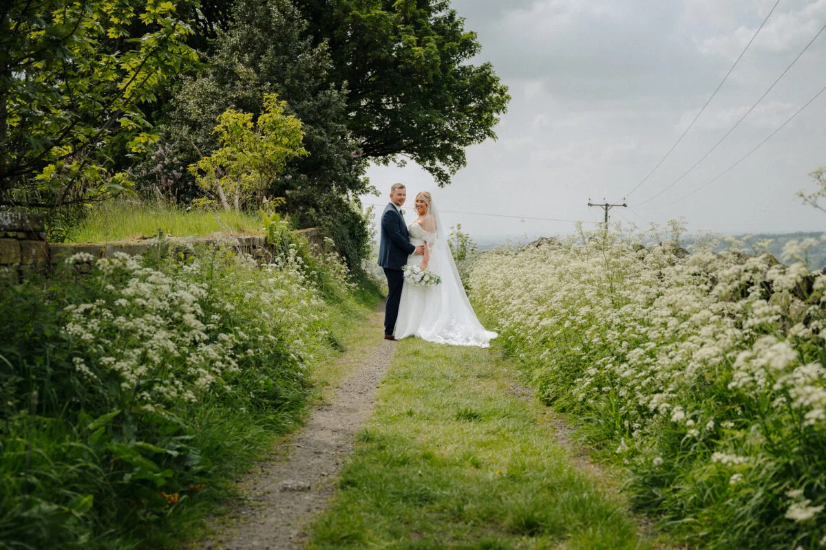 A bride and groom standing on a path in a field.