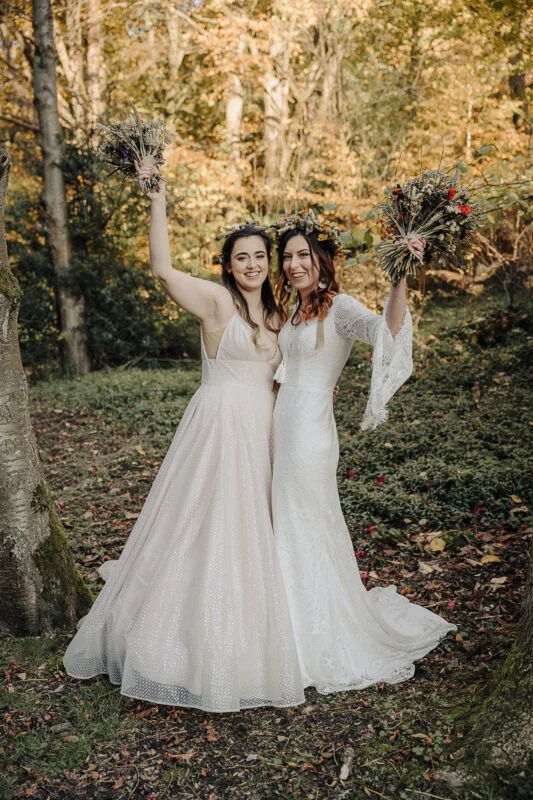 Two brides posing for a photo in the woods.