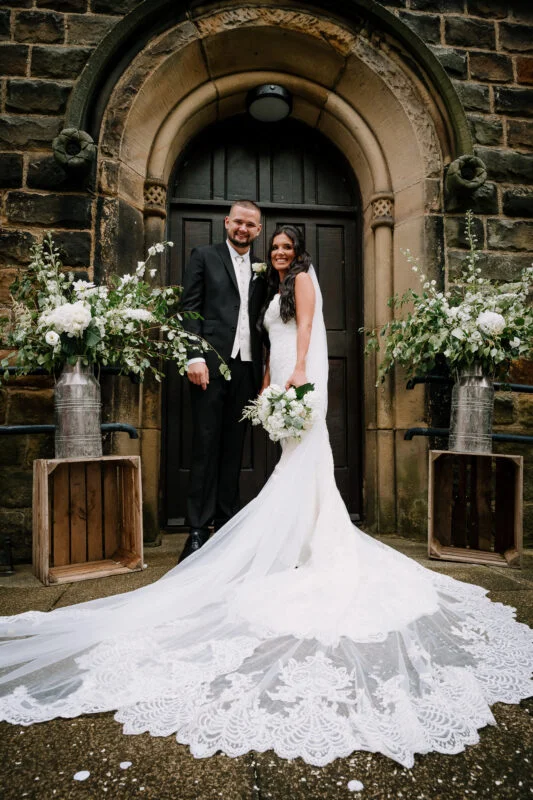 A bride and groom posing in front of an old stone building.