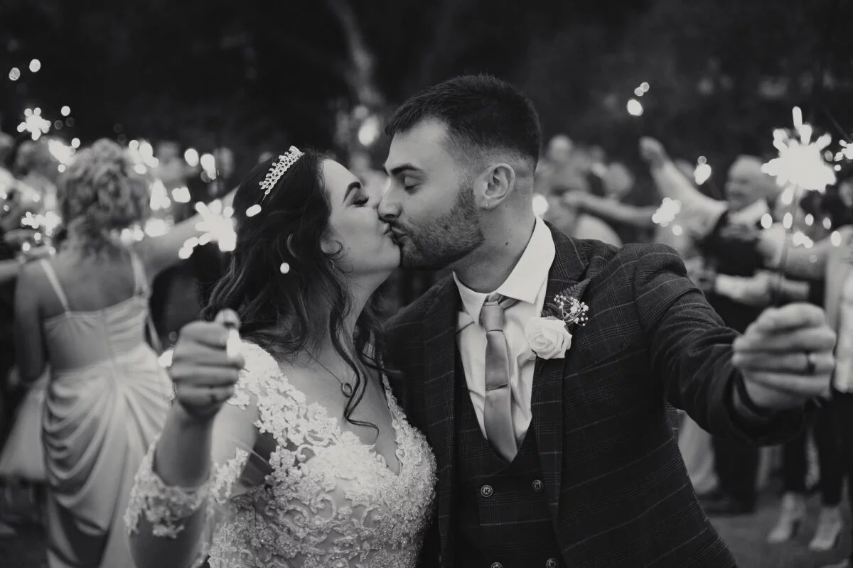Black and white photo of bride and groom kissing with sparklers.