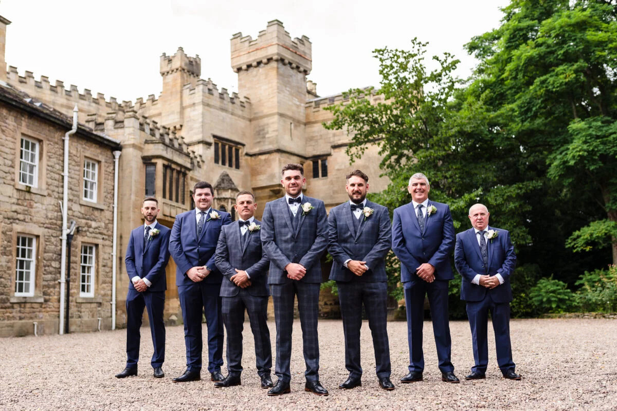A group of groomsmen standing in front of a castle.