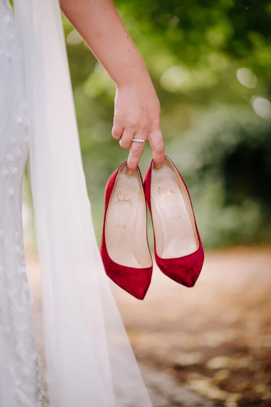 A bride's hand holding a pair of red heels.