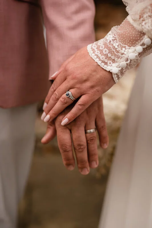 A bride and groom's hands holding each other's wedding rings.