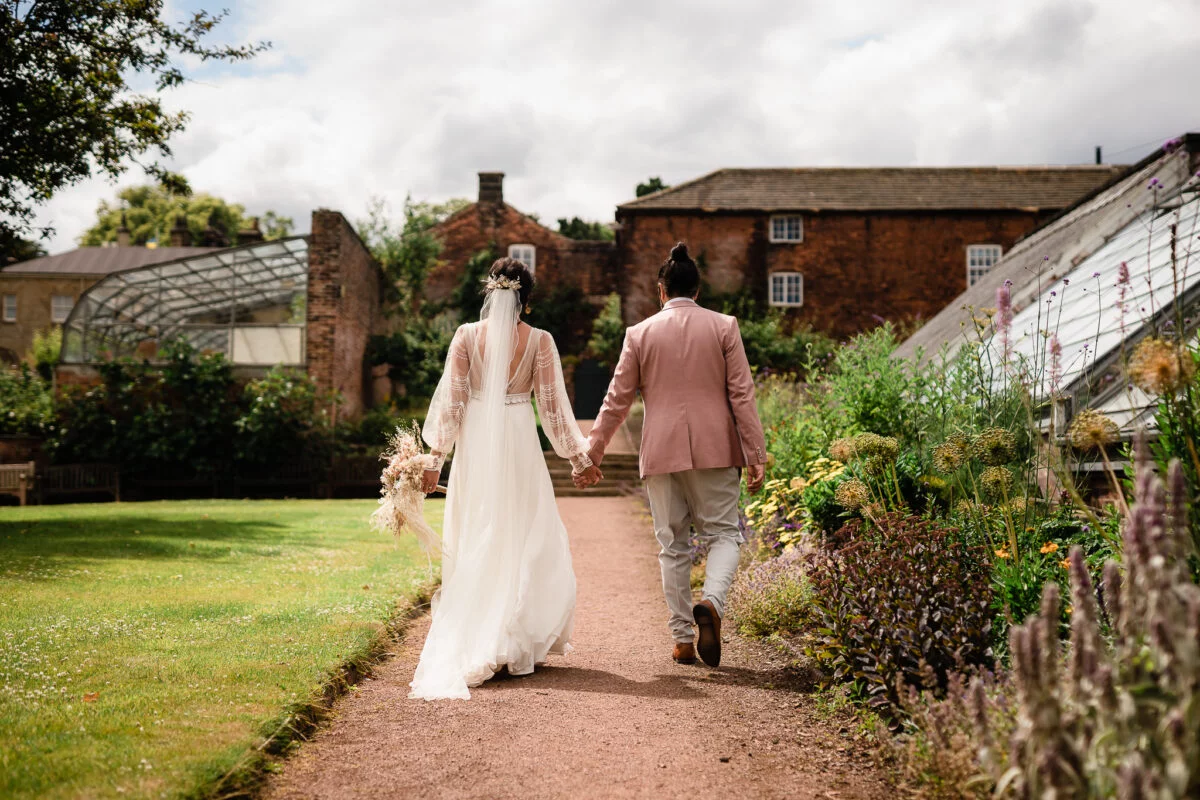 A bride and groom walking down a path in a garden.