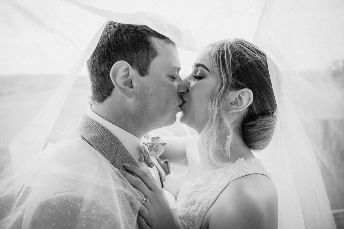 A bride and groom kiss under a veil.