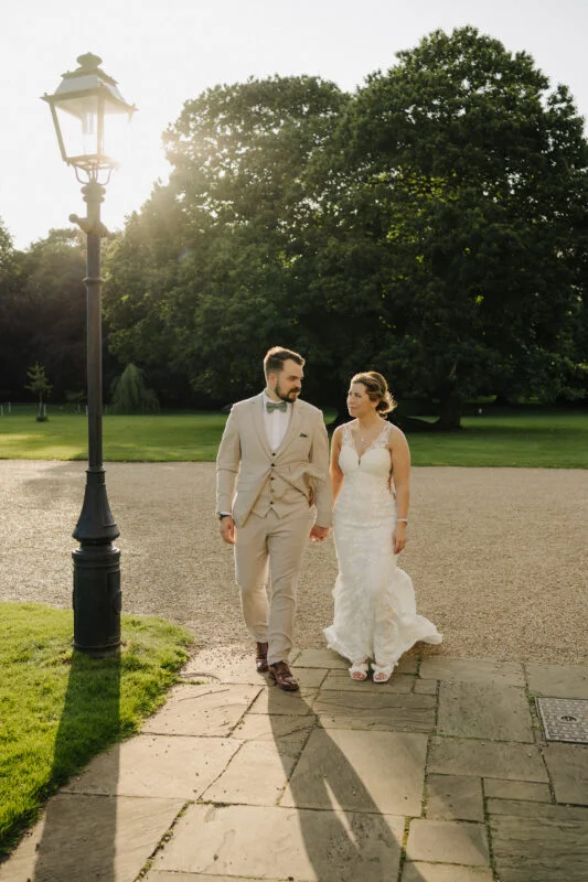 A bride and groom walking down a path in a park.