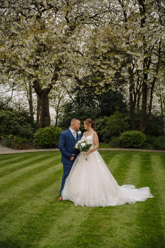 A bride and groom posing in front of a flowering tree.