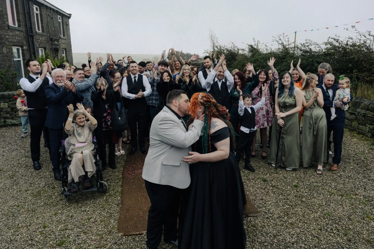 A bride and groom kiss in front of a large group of people.