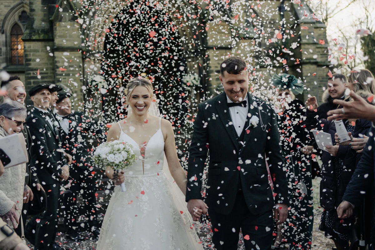 A bride and groom walk through confetti at their wedding.