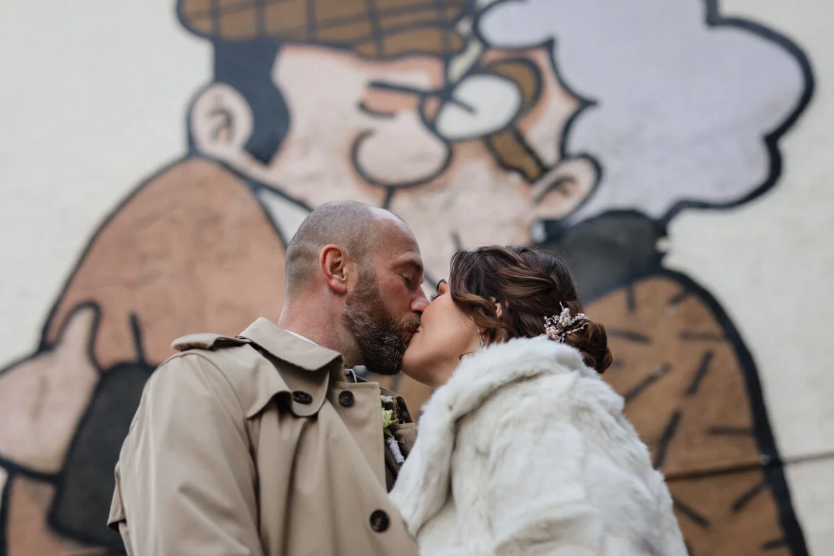 A bride and groom kiss in front of a mural.