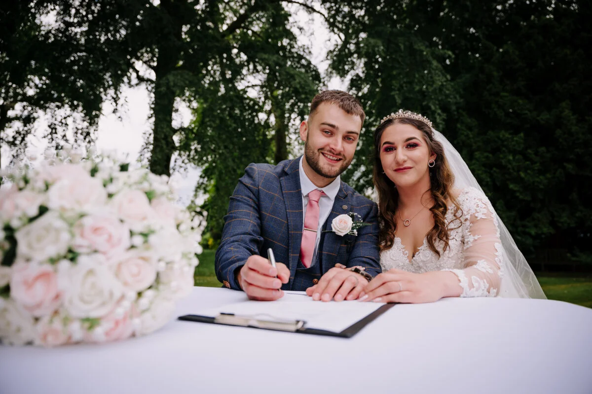 A bride and groom signing their wedding vows at a table.