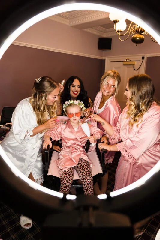 A group of women in pink robes are getting ready in a mirror.