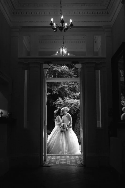 Two brides in wedding dresses standing in an open doorway.