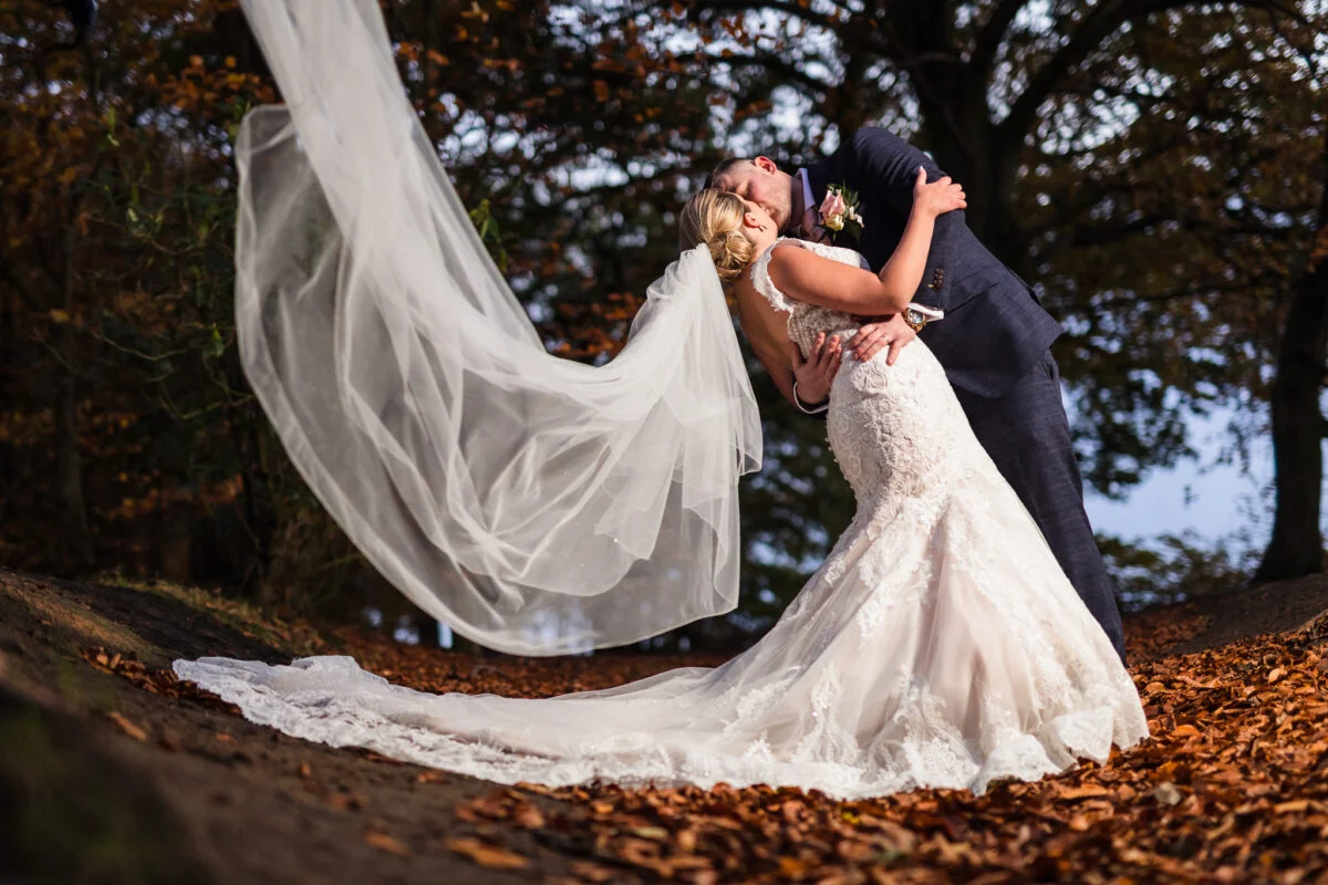 A bride and groom kissing in the autumn leaves.