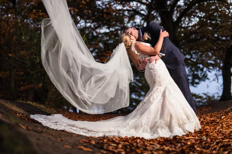 A bride and groom kissing in the autumn leaves.