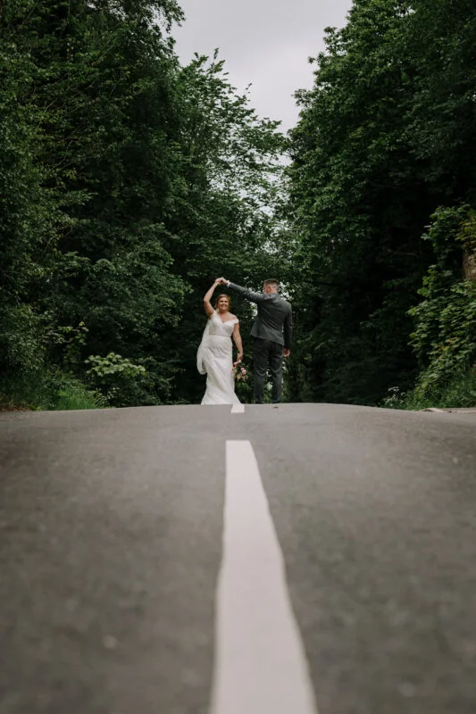 A bride and groom walking down a road in the woods.