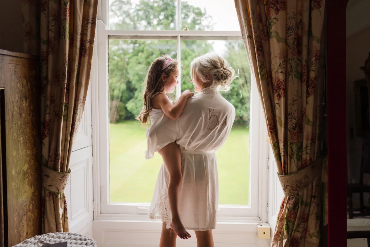 A woman in a robe and a little girl looking out of a window.