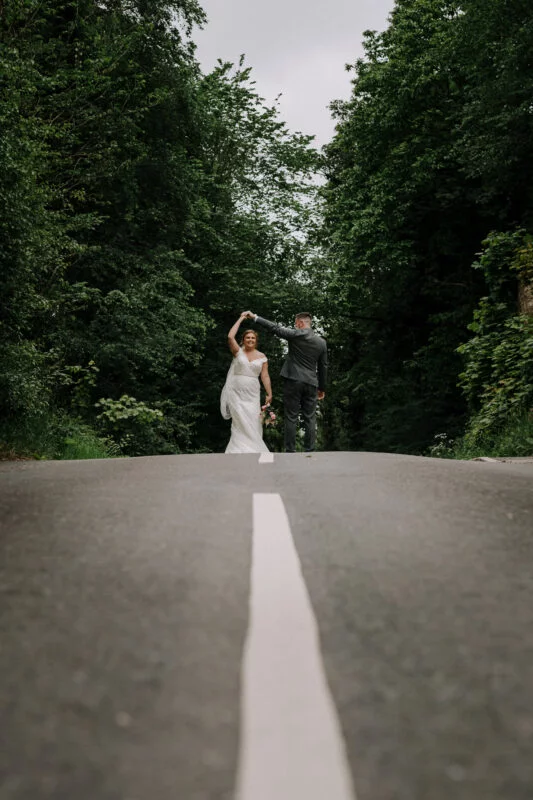 A bride and groom walking down a road in the woods.
