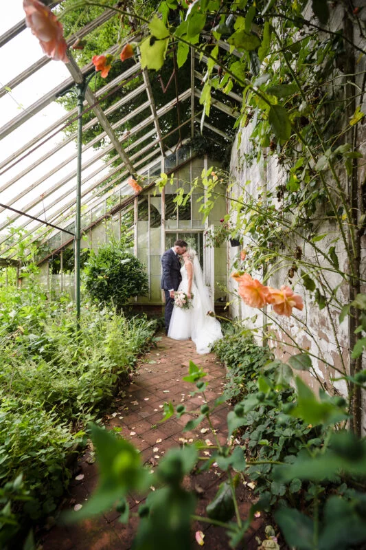 A bride and groom standing in a greenhouse.
