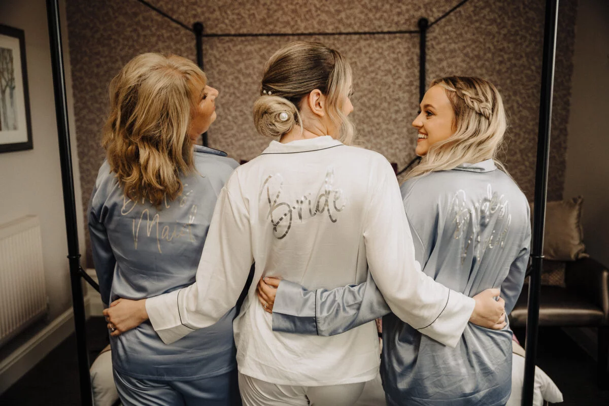 Three bridesmaids wearing robes in front of a mirror.