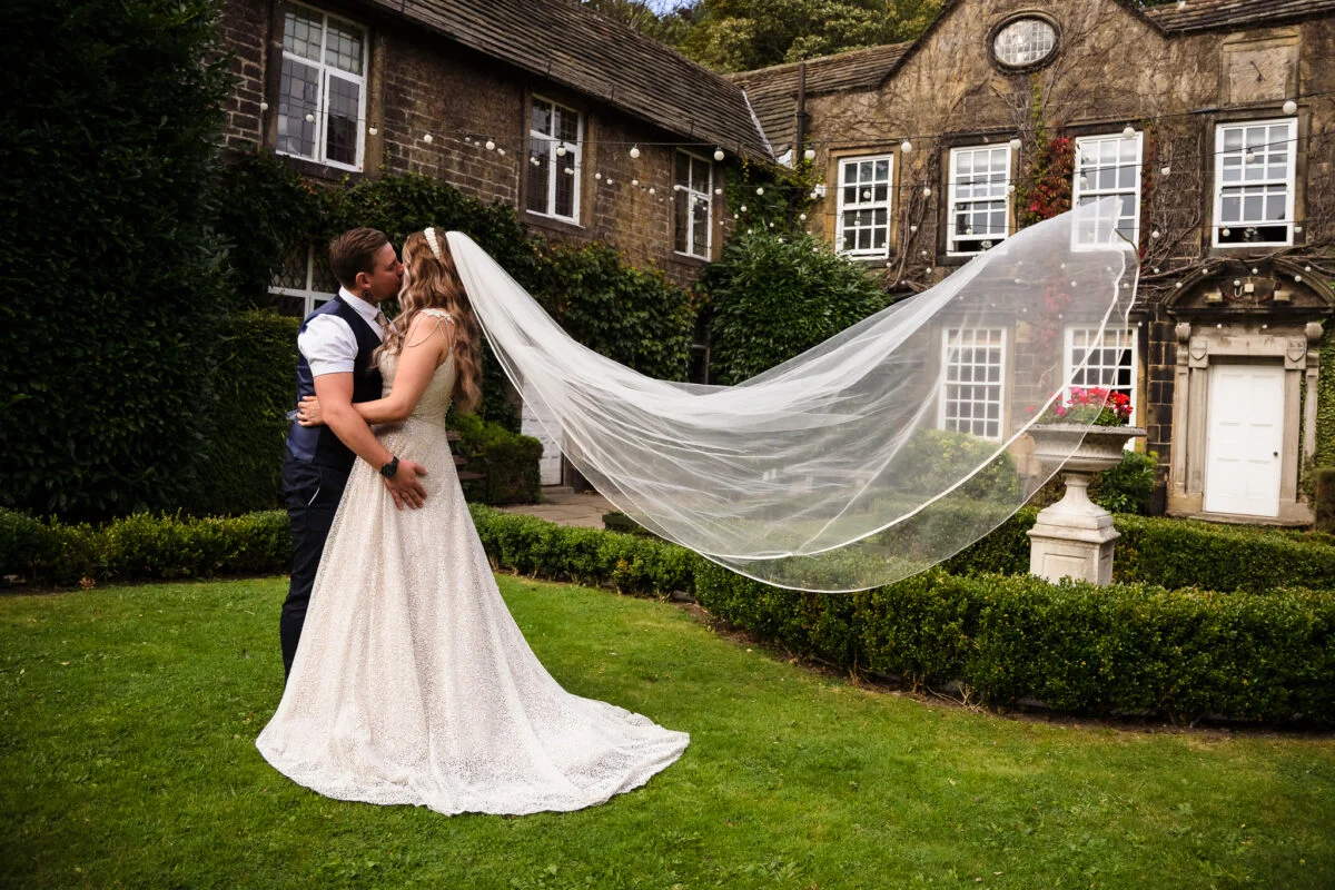 A bride and groom kissing in front of a mansion house.