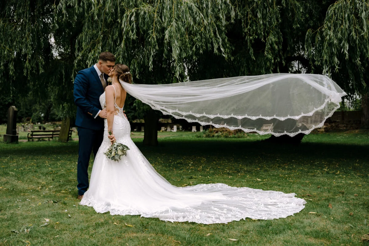 A bride and groom kissing under a willow tree.