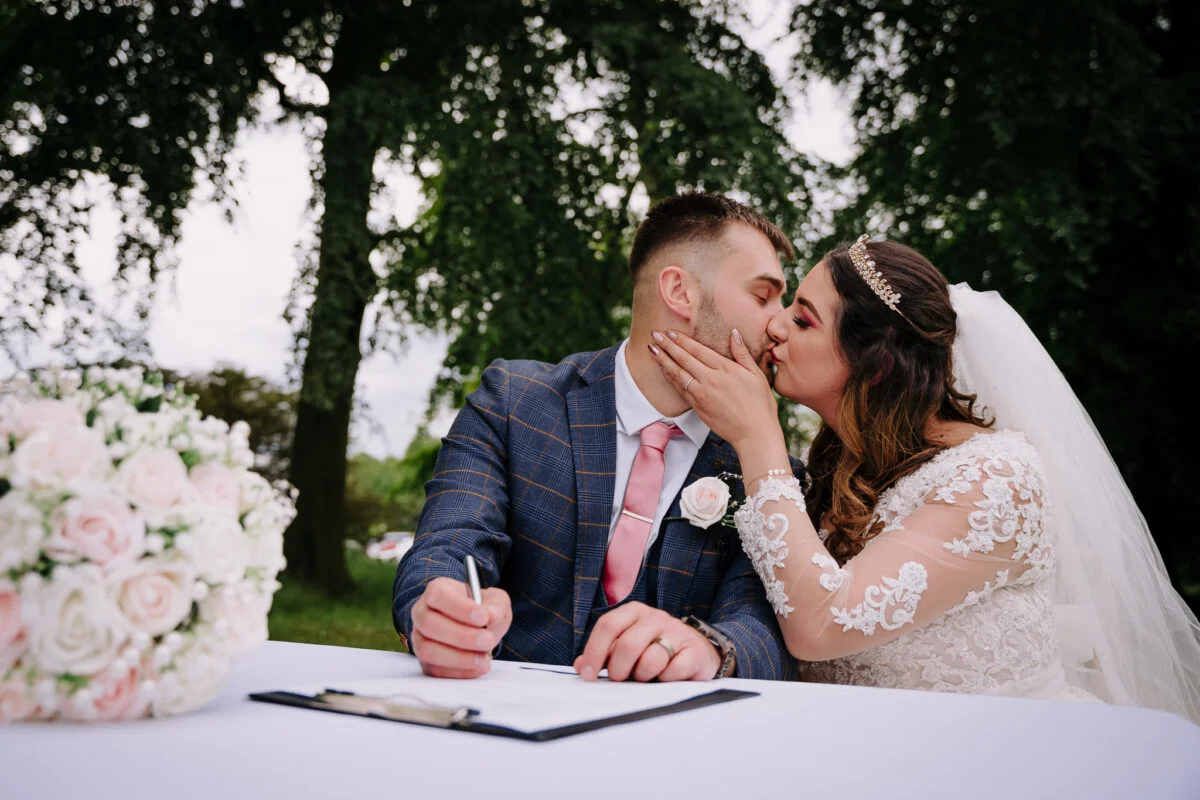 A bride and groom kissing while signing their wedding vows.
