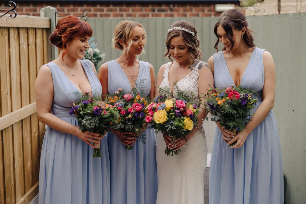 Four bridesmaids holding bouquets in front of a fence.