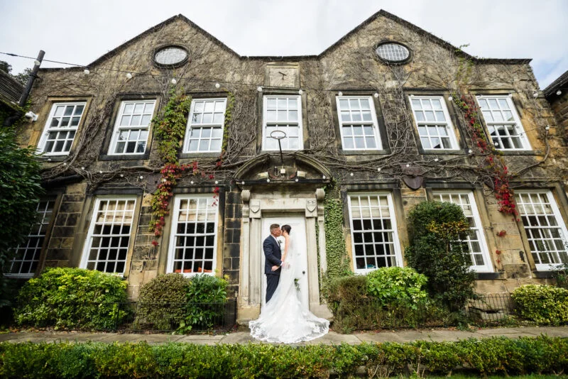 A bride and groom standing in front of an old mansion.