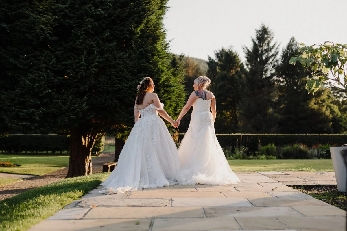 Two brides walking down a path in a garden.