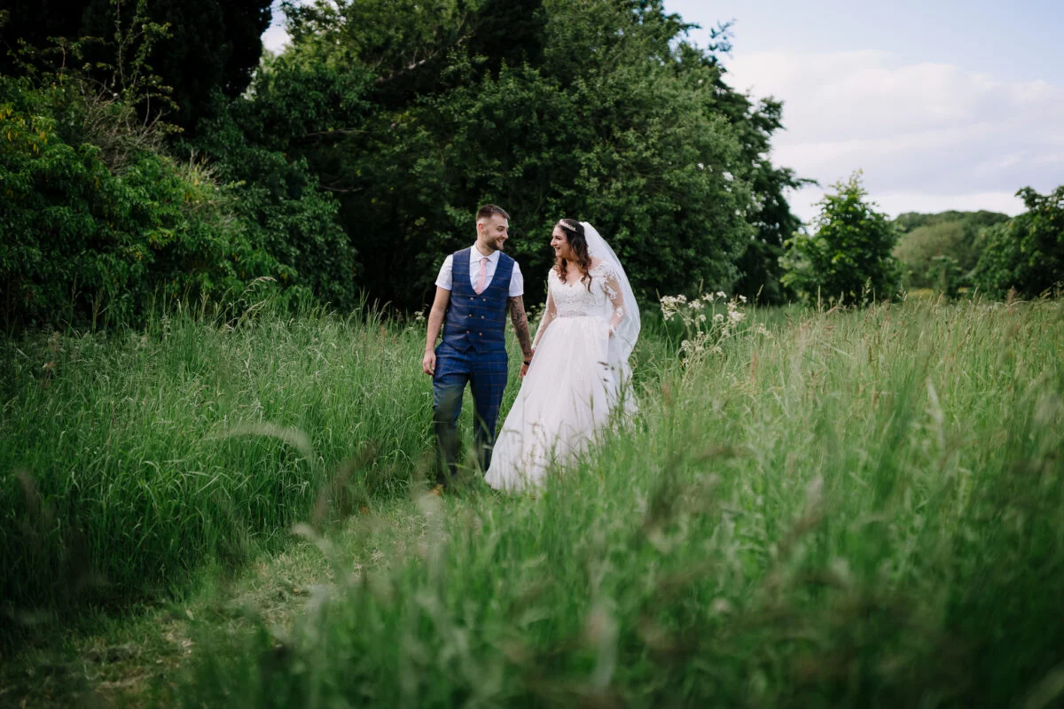 A bride and groom walking through tall grass in a field.
