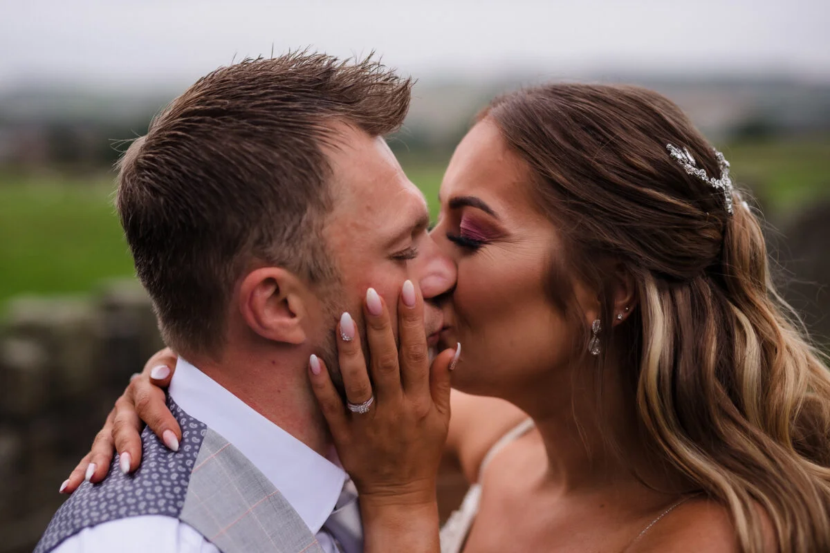 A bride and groom kissing in front of a field.
