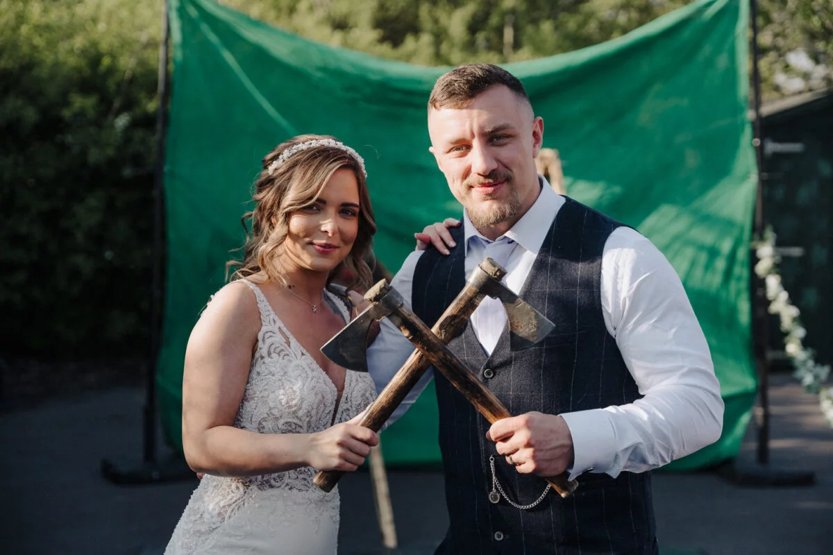 A bride and groom holding axes in front of a green screen.