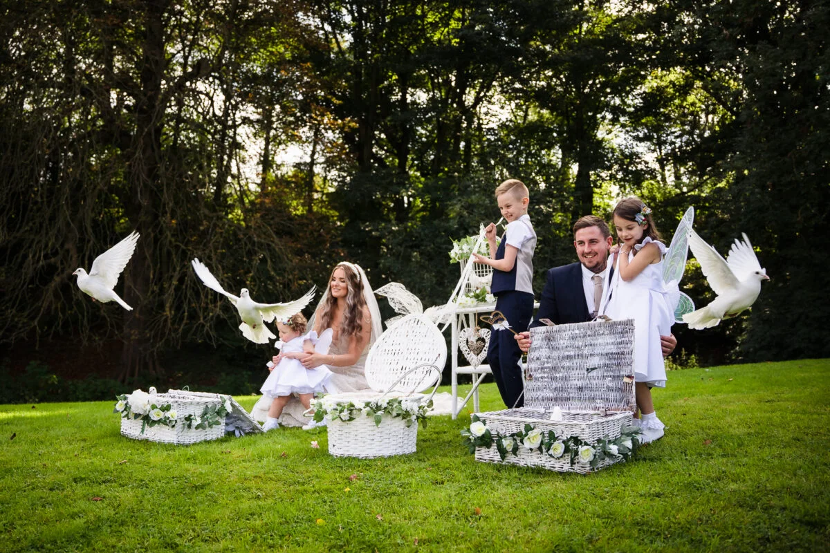 A family posing with white doves in the grass.