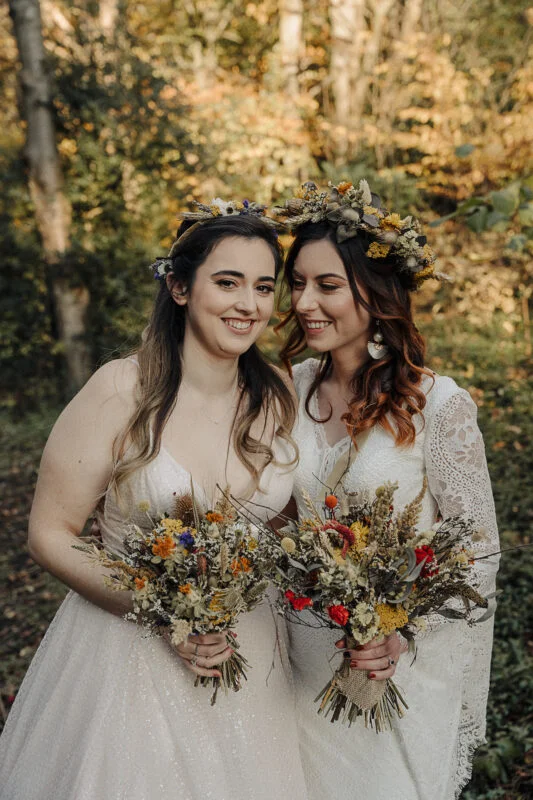 Two brides holding bouquets in the woods.