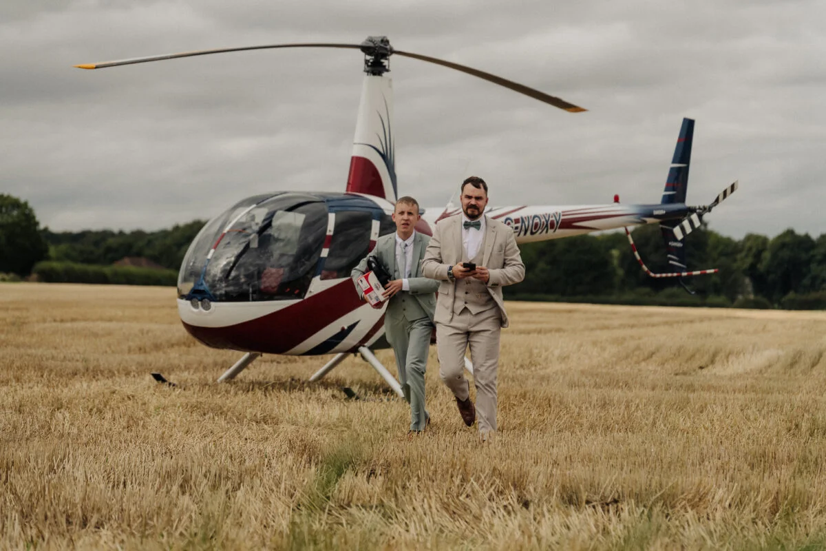 Two men standing next to a helicopter in a field.