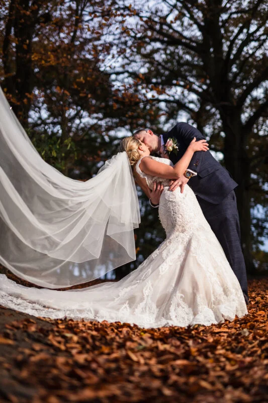 A bride and groom kissing in the autumn leaves.